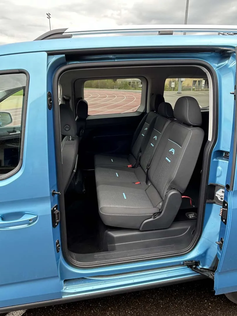 Blauer Kleinbus mit offener Schiebetür zeigt graue Rückbank im Innenraum.
