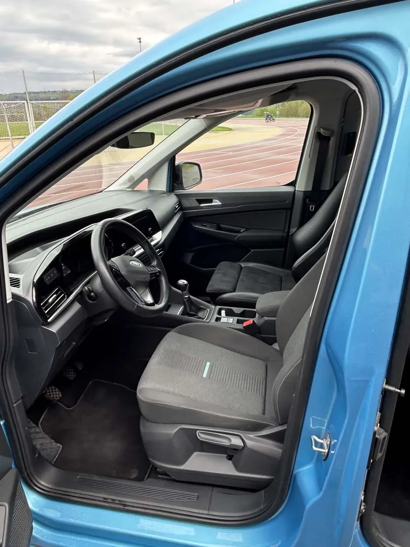 Innenansicht eines blauen Autos mit offener Tür, Lenkrad und Vordersitz sichtbar.