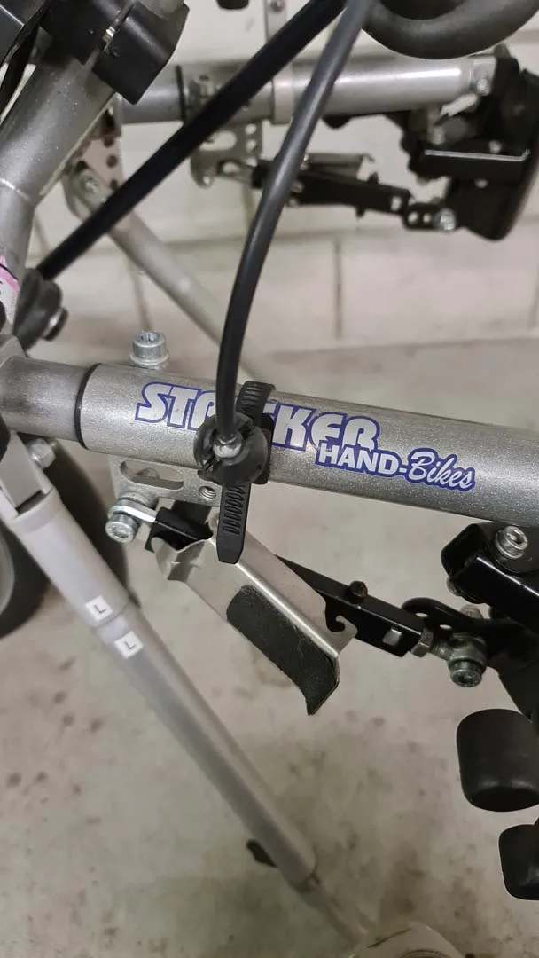 occasion-stricker-vorspannbike-nguyen-02.jpg Zusammengeklappter silberner Rollstuhl mit blauem "M48" Logo auf dem Rahmen.