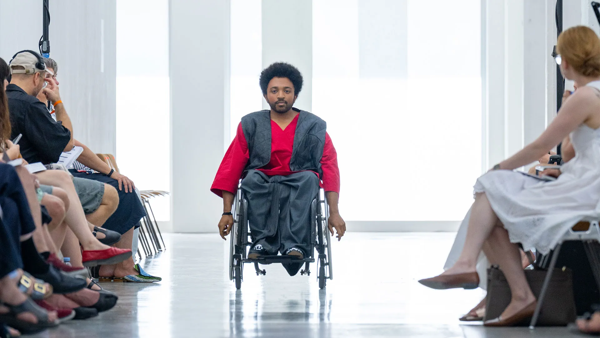 Man in wheelchair wearing red jacket at fashion show.