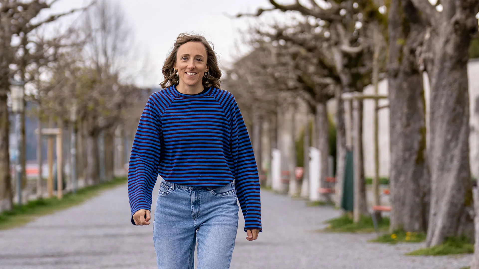Woman in blue striped sweater walking along tree-lined path