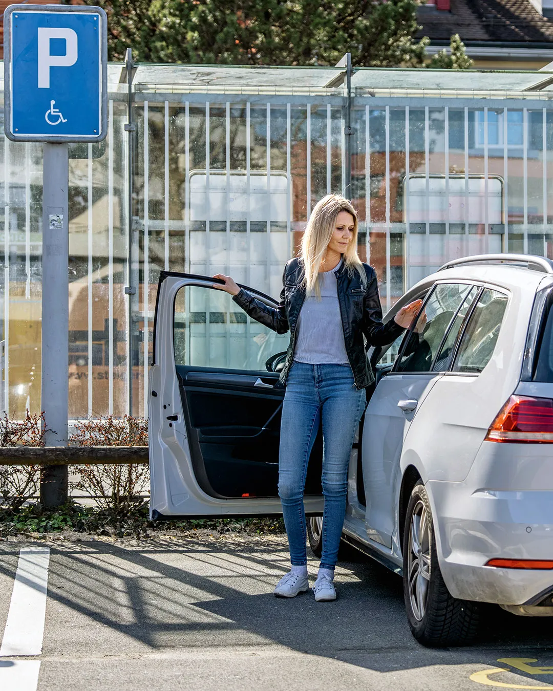 Eine Frau steigt auf einem Rollstuhlparkplatz selbstständig aus dem Auto aus – barrierefreie Mobilität, hindernisfreies Parkieren und Unabhängigkeit im Alltag.