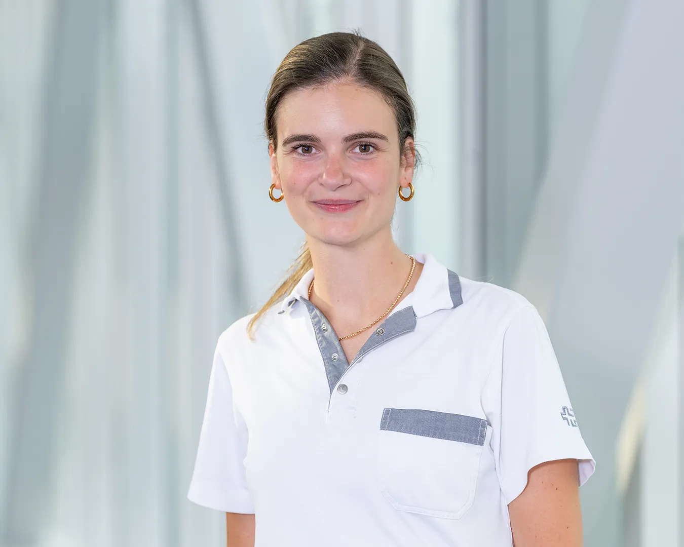 A young woman in a white medical coat, smiling at the camera.