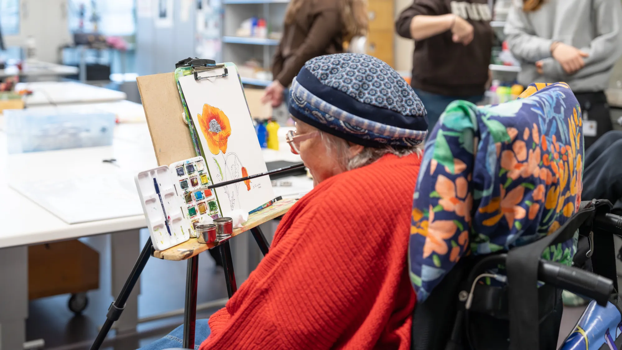 A person wearing a red coat and hat creating artwork in a studio setting.
