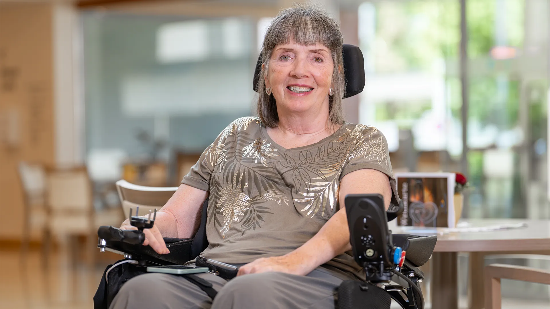 A smiling woman in a wheelchair in a room with a wooden interior.