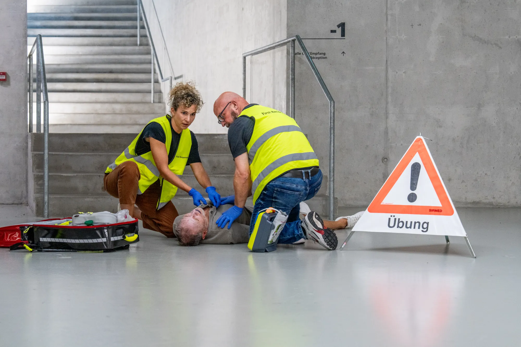 Zwei First Responder in Warnwesten versuchen, einer am Boden liegenden verletzten Person zu helfen.