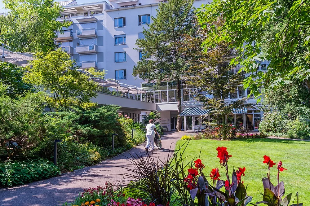 Scenic hotel courtyard with lush greenery, blooming tulips, and a stone path leading to the entrance.
