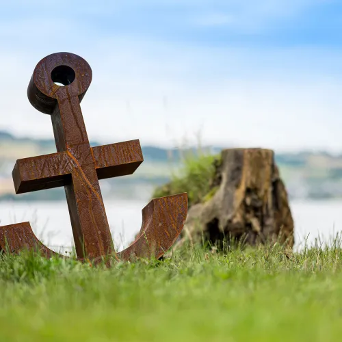 Une ancre rouillée dans un pré. Derrière, on voit le lac de Sempach. 