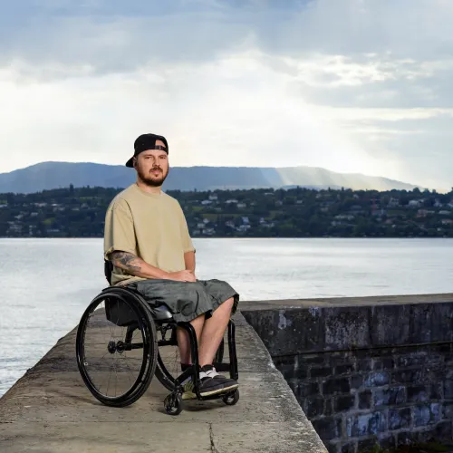 Anton Mityukov sitzt im Rollstuhl auf einem Steg aus Beton mit dem Genfersee im Hintergrund.