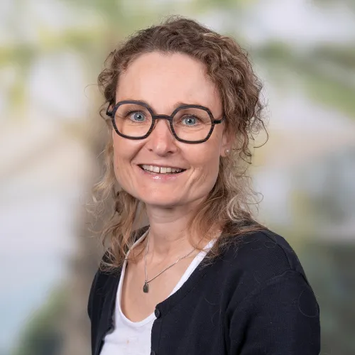 Woman with curly hair and glasses smiling at camera, wearing black cardigan