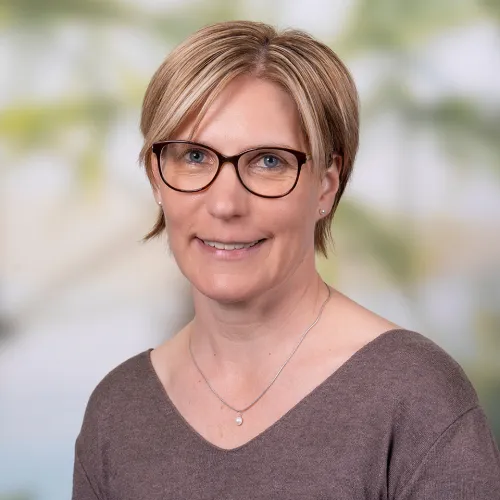 Smiling woman with short blonde hair and glasses wearing a gray sweater