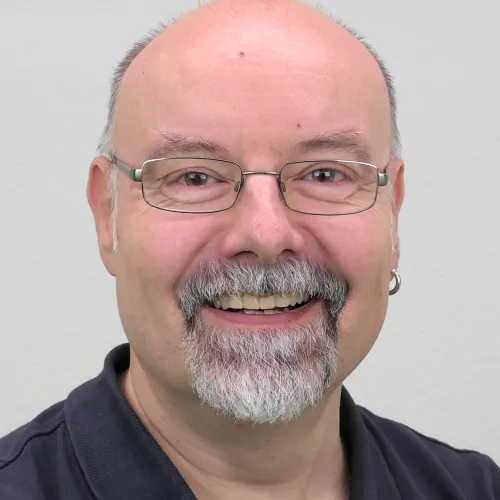Smiling man with glasses and gray beard wearing dark shirt.