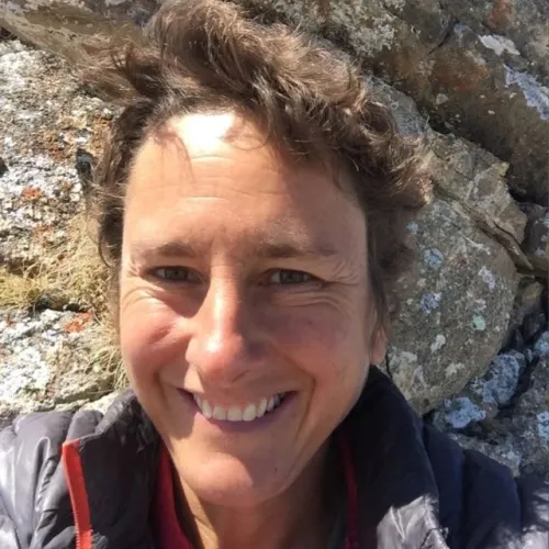 Smiling woman with curly brown hair against a rocky background.