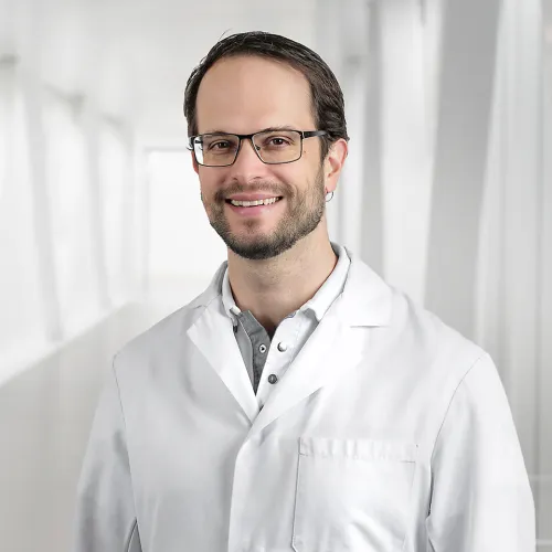 A smiling man in a white lab coat wearing glasses.