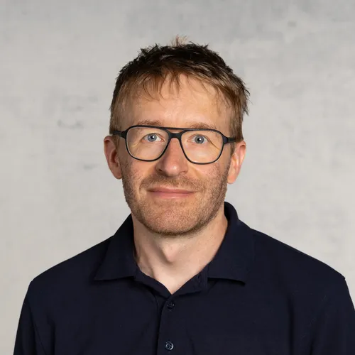 Ein Mann mit Brille und grauen Haaren, der in die Kamera lächelt.