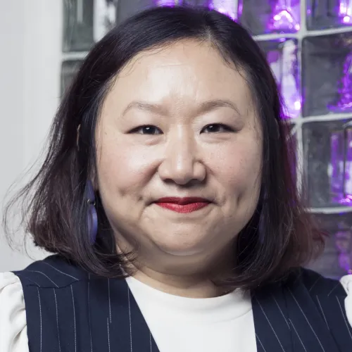 A portrait of a smiling middle-aged Asian woman with dark hair against a colorful background.