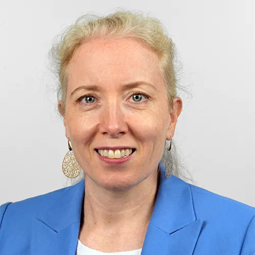 A smiling woman in a blue jacket against a white background.