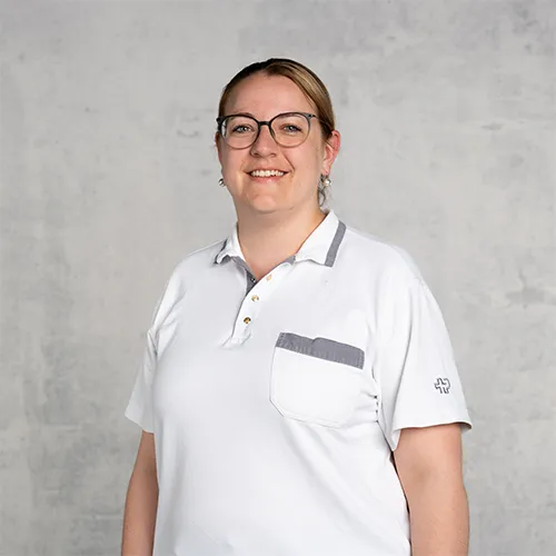 Friendly woman with glasses wearing a white polo shirt, smiling against a gray background.