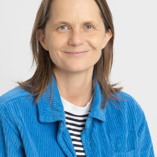 A smiling woman wearing a blue striped sweater and light blue cardigan.