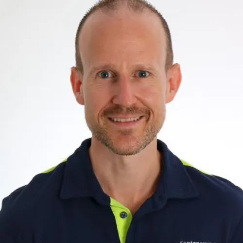 A portrait photograph of a smiling man with short gray hair wearing a navy blue shirt.