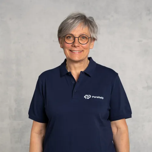 Une femme âgée aux cheveux gris, souriante, portant un polo bleu marine.