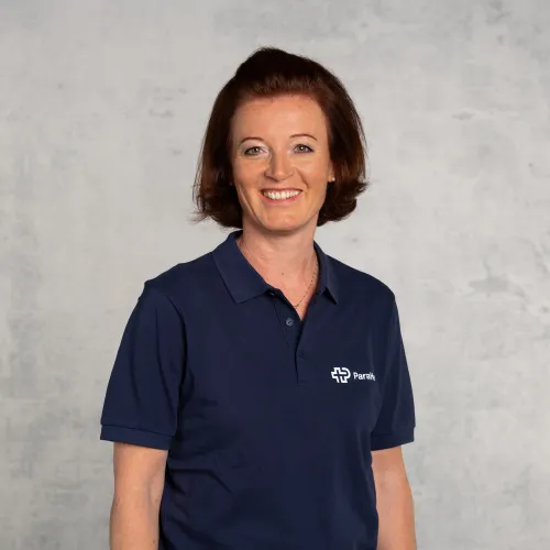 Eine Frau mit braunen Haaren lächelt in die Kamera und trägt ein blaues T-Shirt.