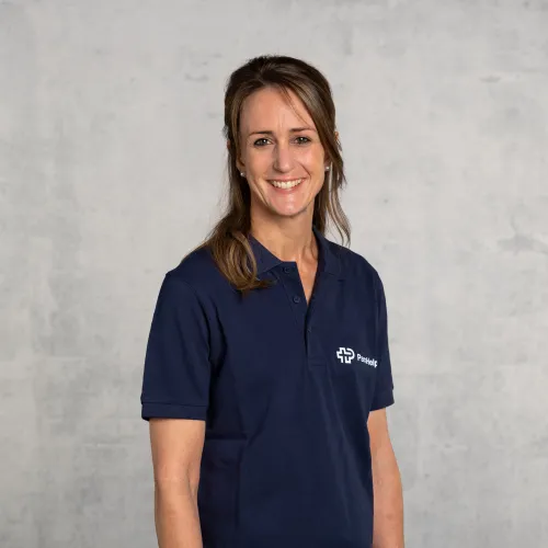 Eine lächelnde Frau in einem blauen Polo-Shirt mit dem Logo einer Organisation.