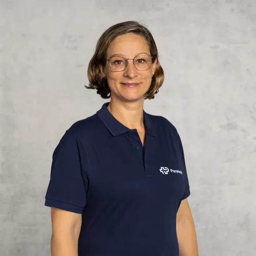 Eine Frau in blauem Polo-Shirt, die in die Kamera lächelt.