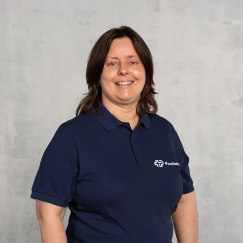 Lachende Frau mit braunen Haaren, die ein dunkelblaues Poloshirt mit einem Logo trägt.