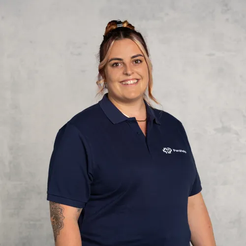 Una donna sorridente con capelli castani raccolti indossa una polo blu navy con il logo dell'azienda.
