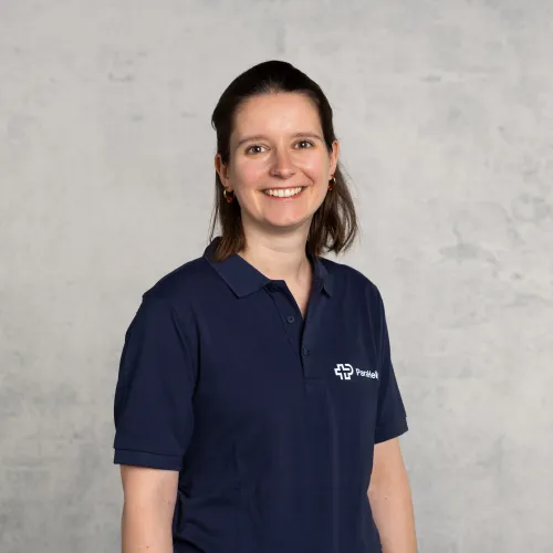 Eine Frau mit lächelndem Gesichtsausdruck, die ein blaues Poloshirt mit einem Firmenlogo trägt.