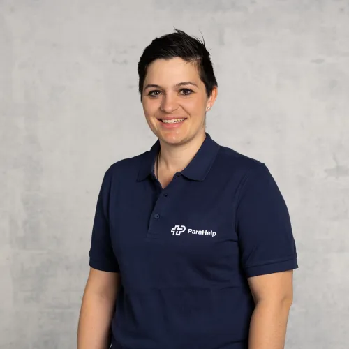 Porträt einer lächelnden Frau in einem blauen T-Shirt mit dem Logo einer Firma.