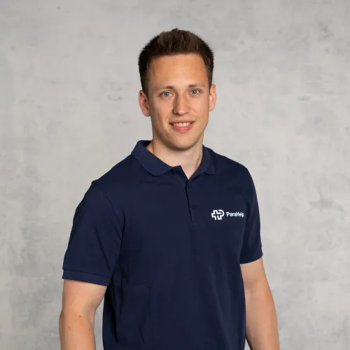 Ein Foto von einem lächelnden Mann mit kurzen braunen Haaren, der ein blaues Hemd mit einem Logo trägt.