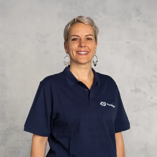 Eine Frau mittleren Alters mit kurzen grauen Haaren, die in einer blauen Uniforinoluft schaut und lächelt.