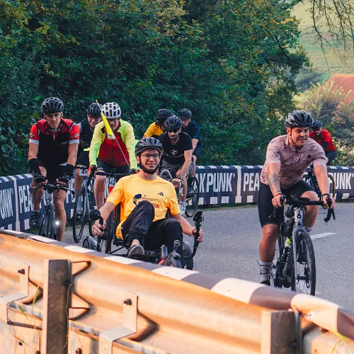 Ein Gruppe von Radfahrern auf einer Brücke in einen Park mit Bäumen im Hintergrund.