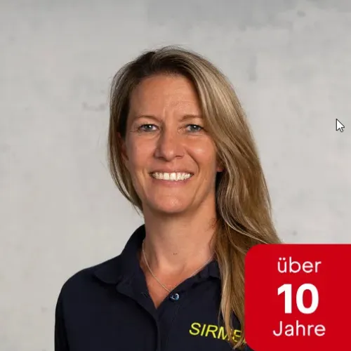 A smiling middle-aged woman with long blond hair, wearing a navy blue collared shirt against a white background.