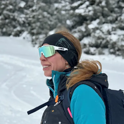 A woman wearing a black helmet and goggles skiing downhill on a snowy slope.