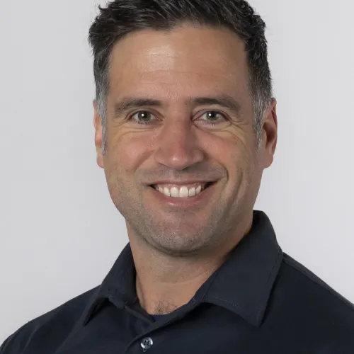 A smiling man with short dark hair wearing a navy blue shirt.